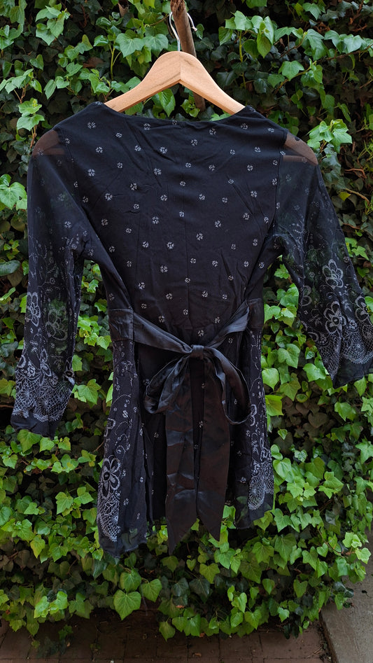 Black dress with white patterns on a mannequin against a green leafy background