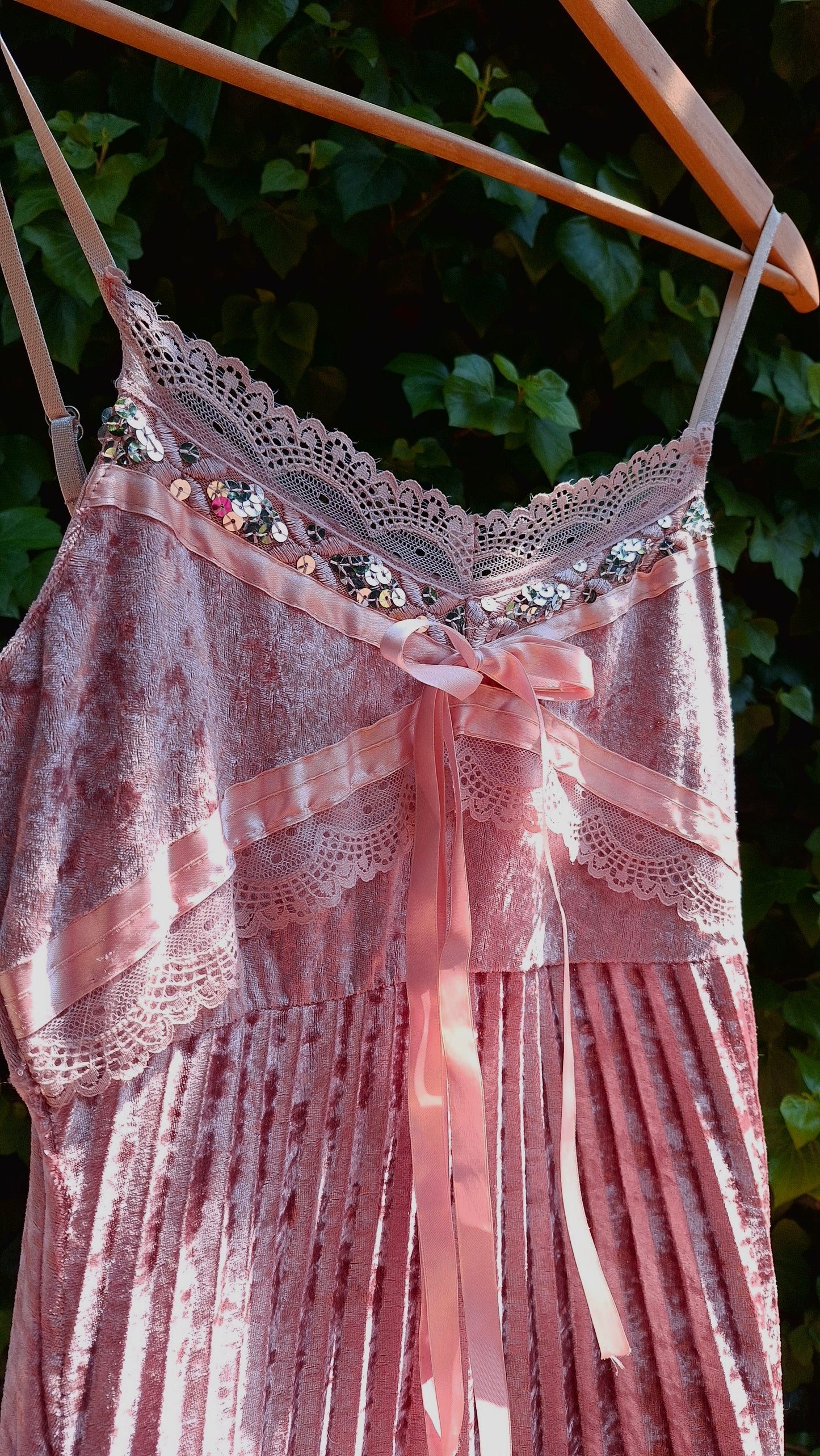 Pink lace dress with pleated details hanging on a clothesline against a green leafy background