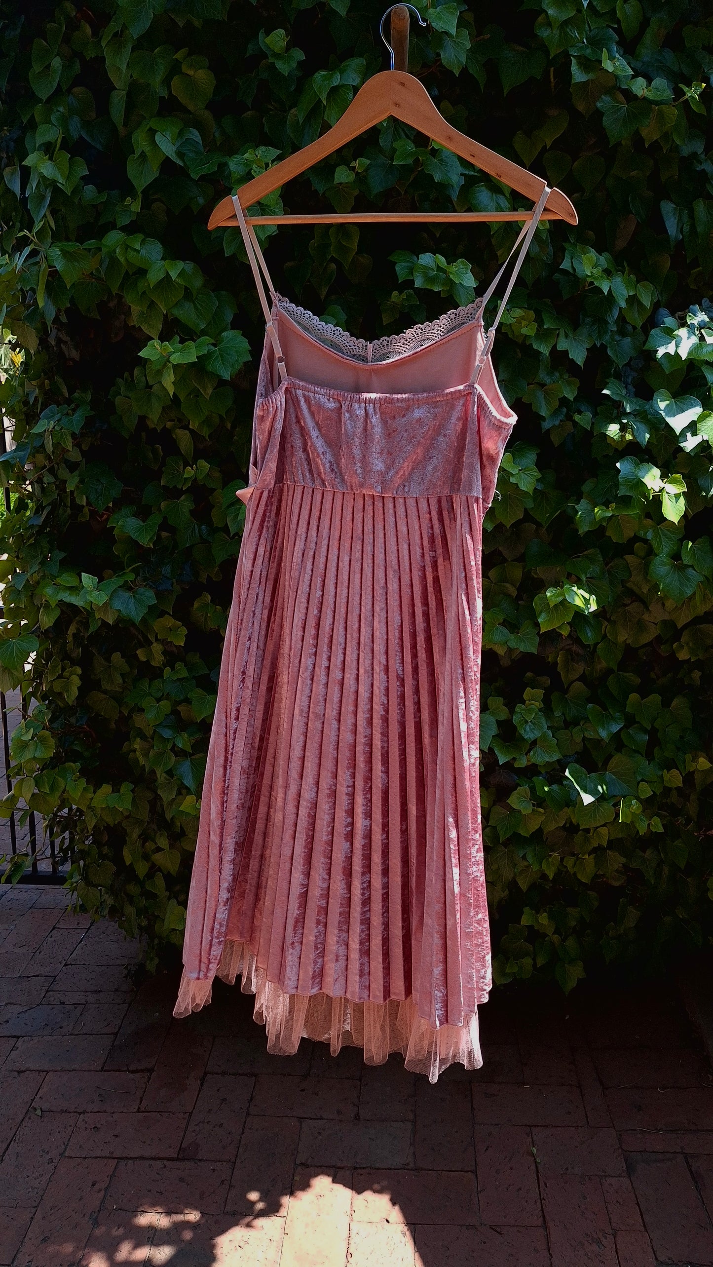 Pink pleated dress on a hanger against a green bush background