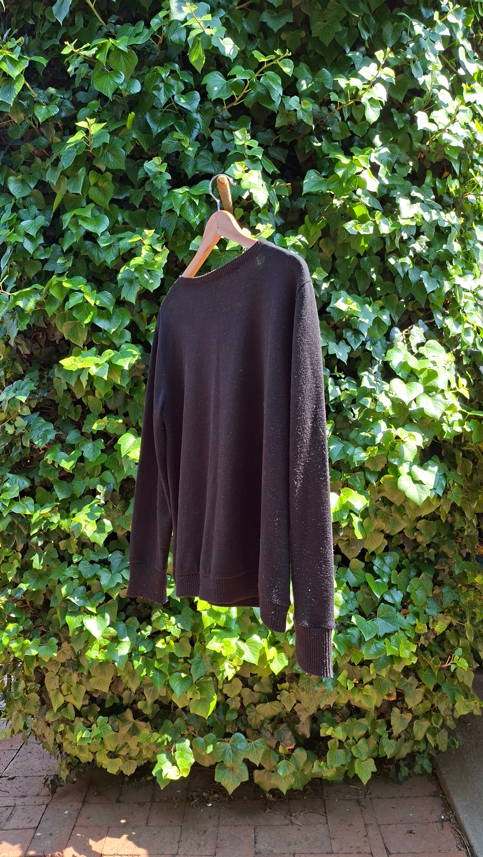 Black sleeveless top held up against a green ivy wall