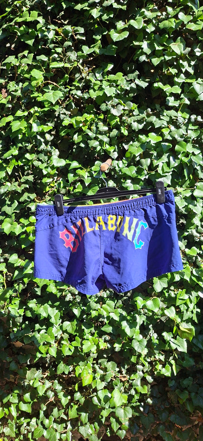 Blue swim brief with branding on a green leafy background